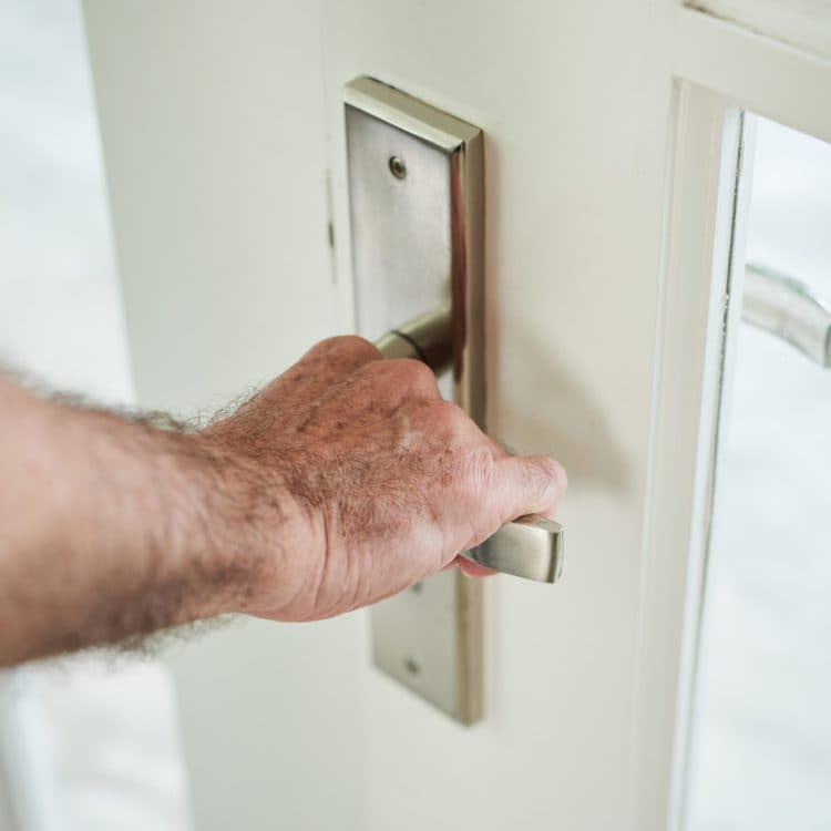 Main posée sur la poignée d'une porte d'entrée fermée